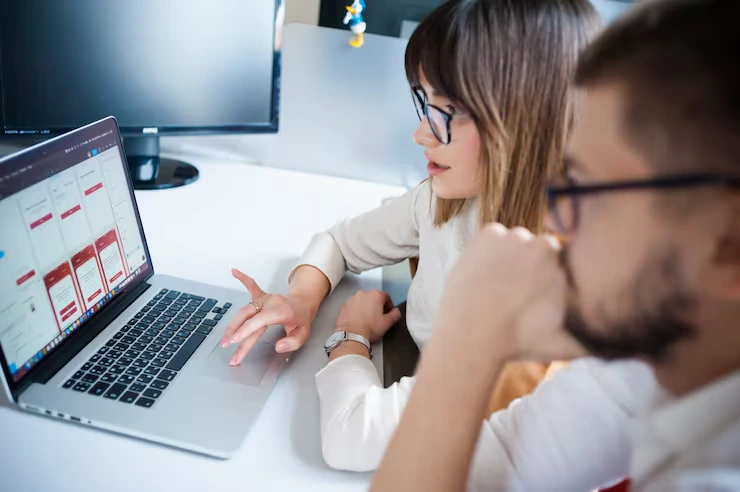 Two professionals analyzing email campaign performance data on laptop screen in modern office