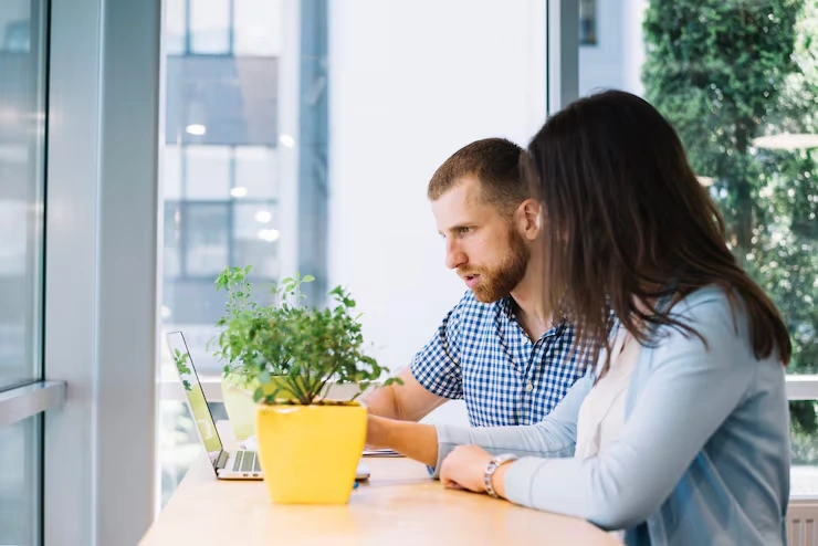 Content strategist and colleague reviewing laptop screen while planning editorial calendar at bright office desk