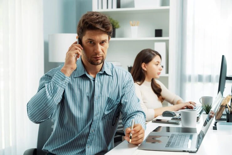 Cold caller conducting live prospect call while colleague updates CRM system in background