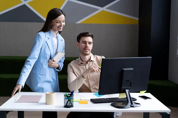Female consultant presenting IT lead generation strategy to male client viewing desktop monitor in modern office
