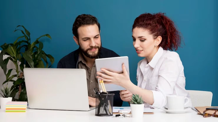 Man and woman reviewing lead data on tablet while collaborating at desk with laptop