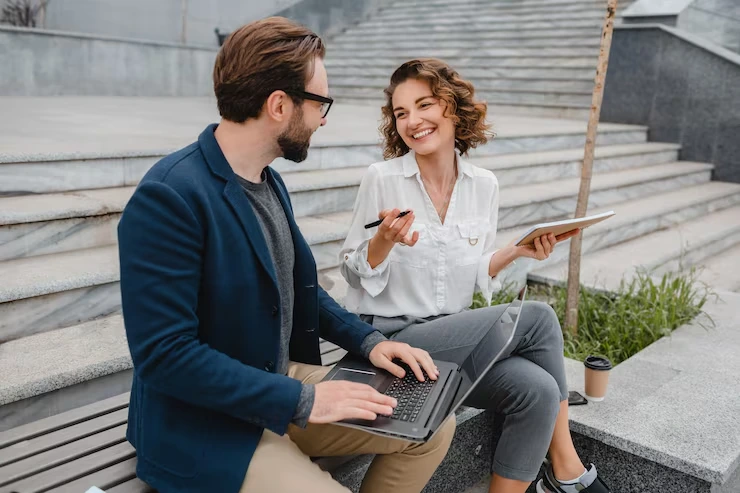Professional woman explaining lead nurturing strategy to man while reviewing data on laptop outdoors