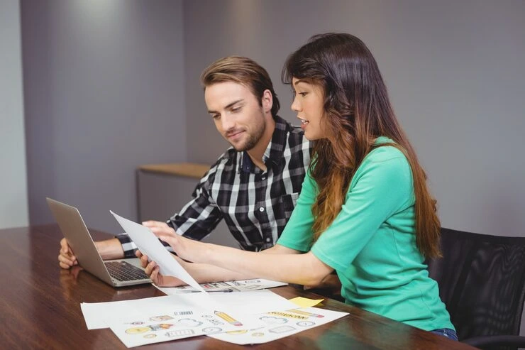 Two professionals reviewing lead research documents and laptop data during strategy session