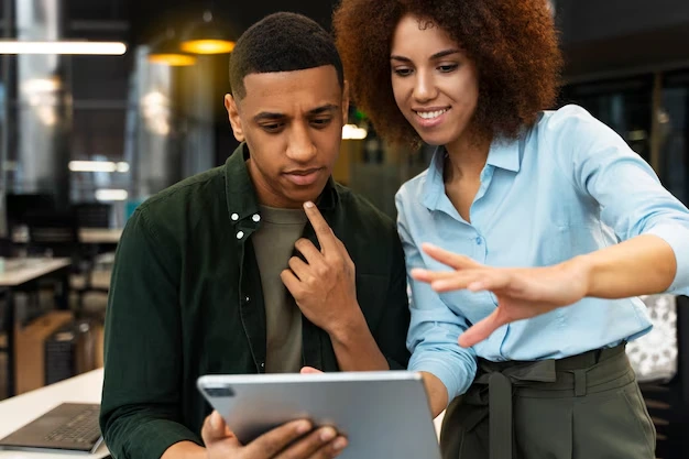 Marketing strategist presenting tablet campaign data to colleague in modern office workspace