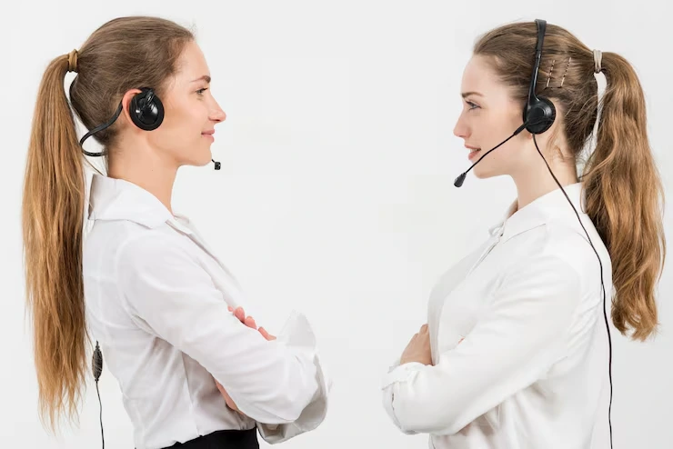 Two call center professionals wearing headsets facing each other in white business attire