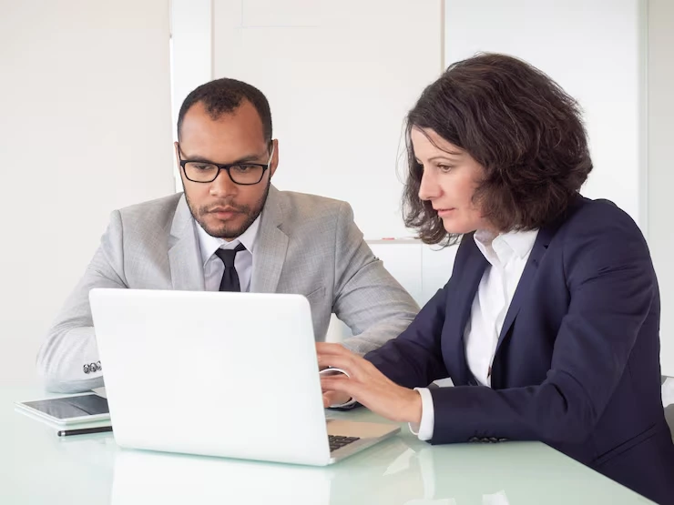 Two business professionals reviewing IT lead generation strategy on laptop during consultation meeting