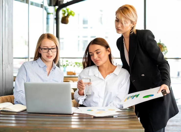 Three women reviewing charts and laptop at café table
